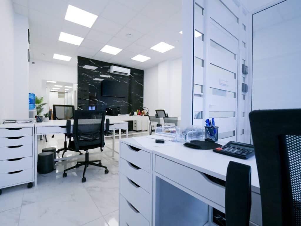 Intérieur d'agence immobilière avec bureaux blancs à tiroirs, cloisons vitrées et mur en marbre noir