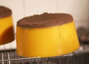 Pain de cire d'abeille pure fondue et démoulée, de couleur jaune orangé, dont le dessus retient les impuretés brunes, posé sur une grille