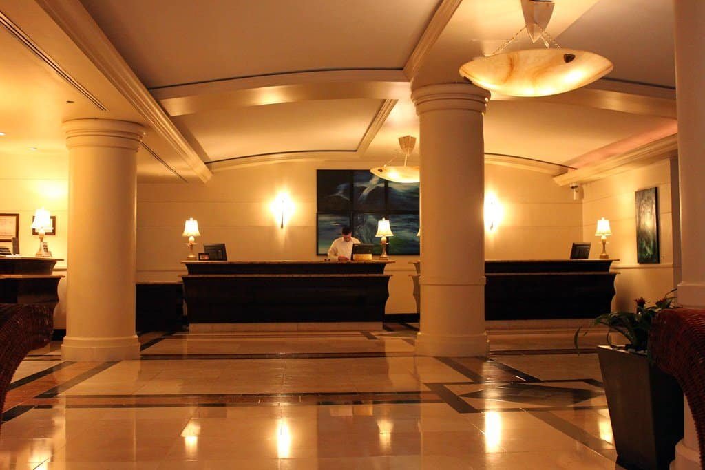 Hall d'hôtel avec longue banque de réception en bois sombre, colonnes et lampes de table