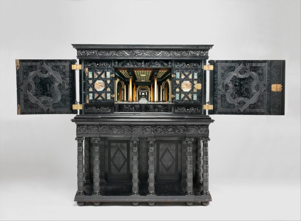 Cabinet d'ébène français ouvert, vantaux sculptés de motifs géométriques, intérieur en perspective architecturale avec colonnes et marqueterie, reposant sur un piètement à colonnes