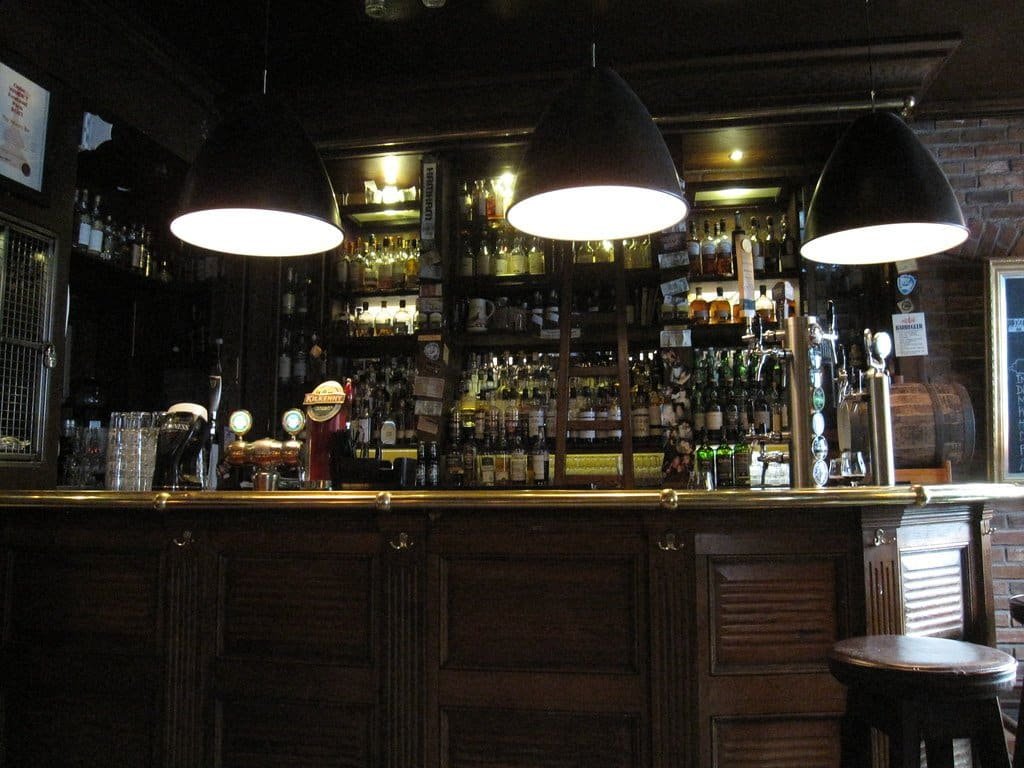 Comptoir de bar en bois sombre à panneaux, arrière-bar garni de bouteilles et suspensions noires