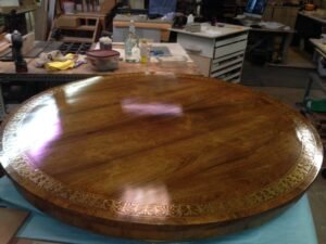 Plateau de table ronde en bois de rose à filet de laiton incrusté, au vernis au tampon miroitant, posé sur un établi dans un atelier d'ébénisterie